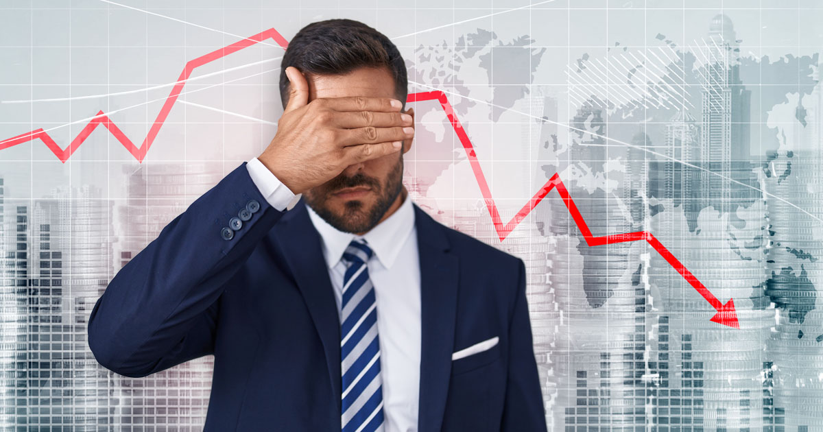 A man covering his eyes as the stock market falls in the background