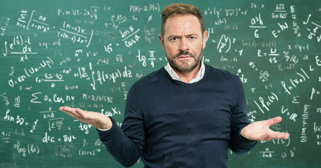 A man shrugging in front of a chalkboard covered with math equations